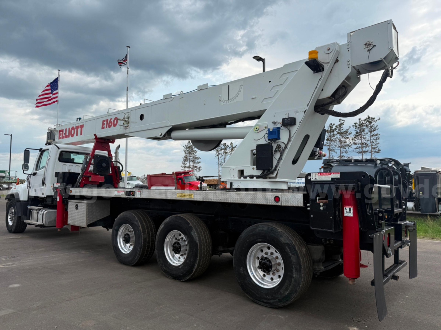Freightliner 114SD boom truck shown in side profile with extendable boom folded overhead and multiple axles.