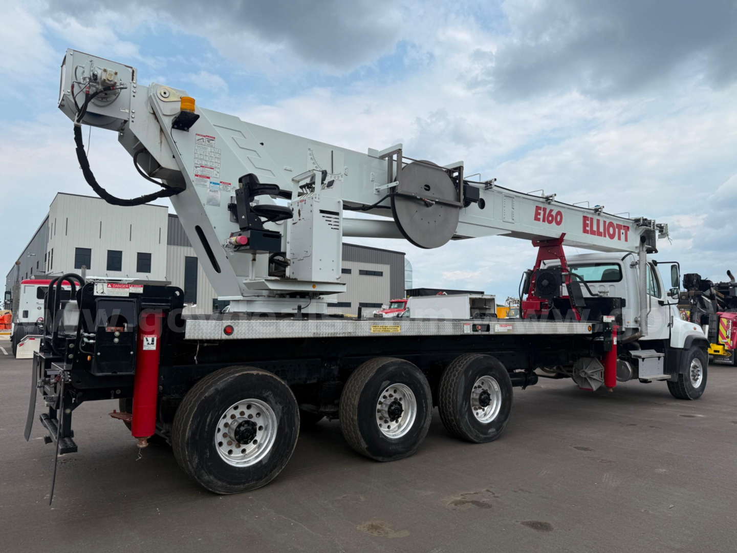 Truck-mounted crane on a Freightliner 114SD with long flatbed; equipment labels and crane arm visible, including E160 and ELLIOTT branding on the crane.
