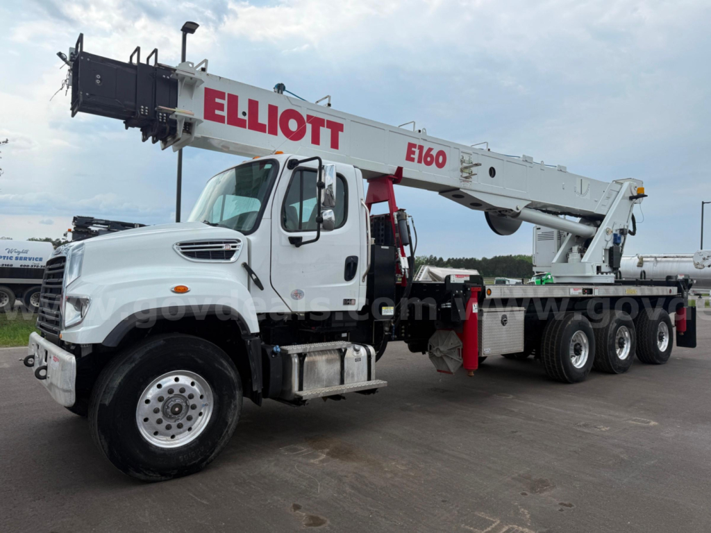 Heavy-duty boom truck with white cab and extended gray crane labeled E160, red Elliott branding on boom, multiple axles, side steps, and storage compartments.