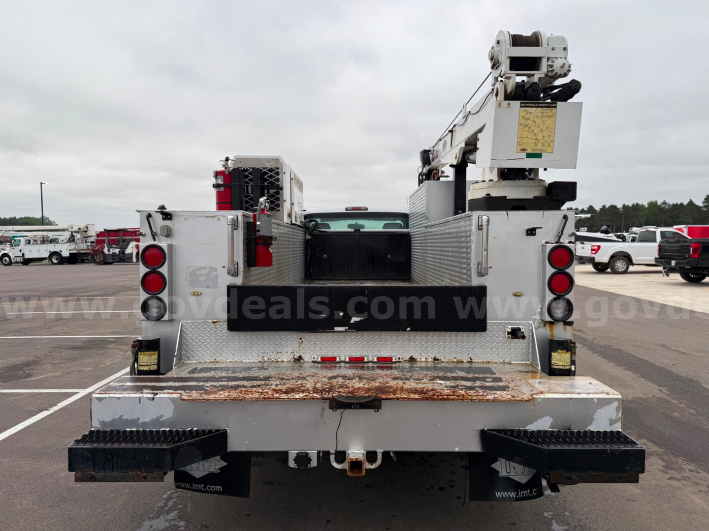 Rear view of a 2011 Ford F550 service/utility truck with flatbed and equipment racks, showing dual rear lights, bumper steps, and a crane/boom on the bed.