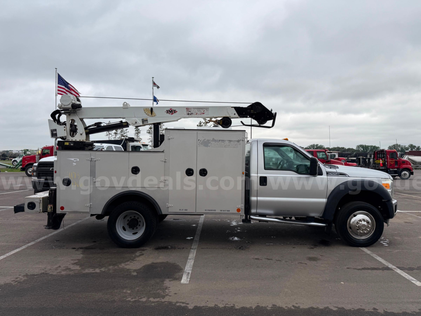 Ford F-550 utility service truck in a parking lot, side view showing service body with compartments, crane arm on top and American flag in rear.