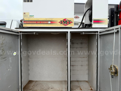 Utility/service body compartments open with three vertical storage bays on a ford f550, interior metal walls showing some rust and wear, hydraulic equipment visible above.