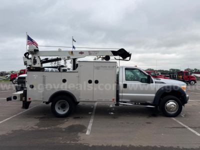 Ford F-550 utility service truck in a parking lot, side view showing service body with compartments, crane arm on top and American flag in rear.