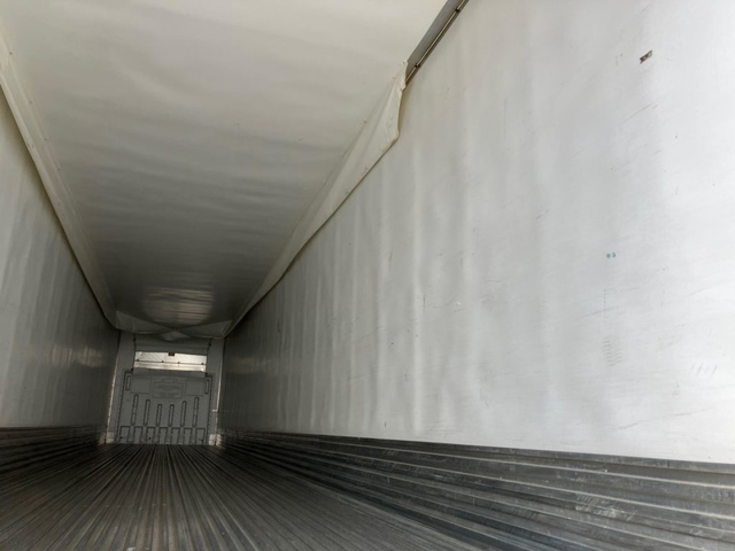 Trailer interior showing a long refrigerated trailer cargo area with ribbed floor, white walls, and a rear doorway.