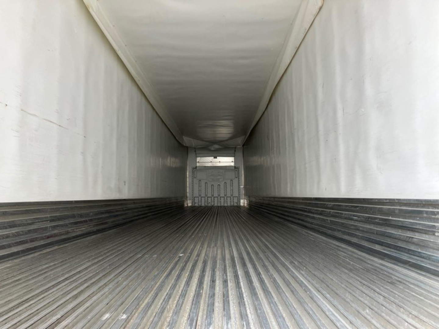 Trailer interior showing corrugated metal floor with ridges, white sidewalls, and a rear door opening at far end.