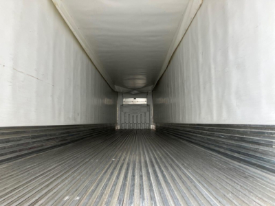 Trailer interior showing corrugated metal floor with ridges, white sidewalls, and a rear door opening at far end.