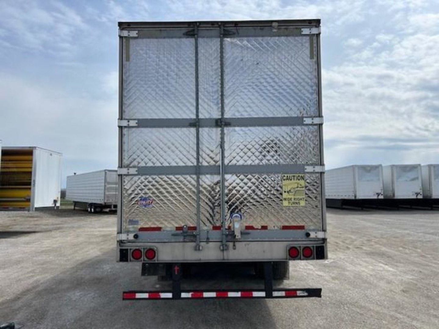 Rear view of a 2019 Utility refrigerated trailer with diamond plate aluminum doors, safety decals, and red/white rear underride guard.