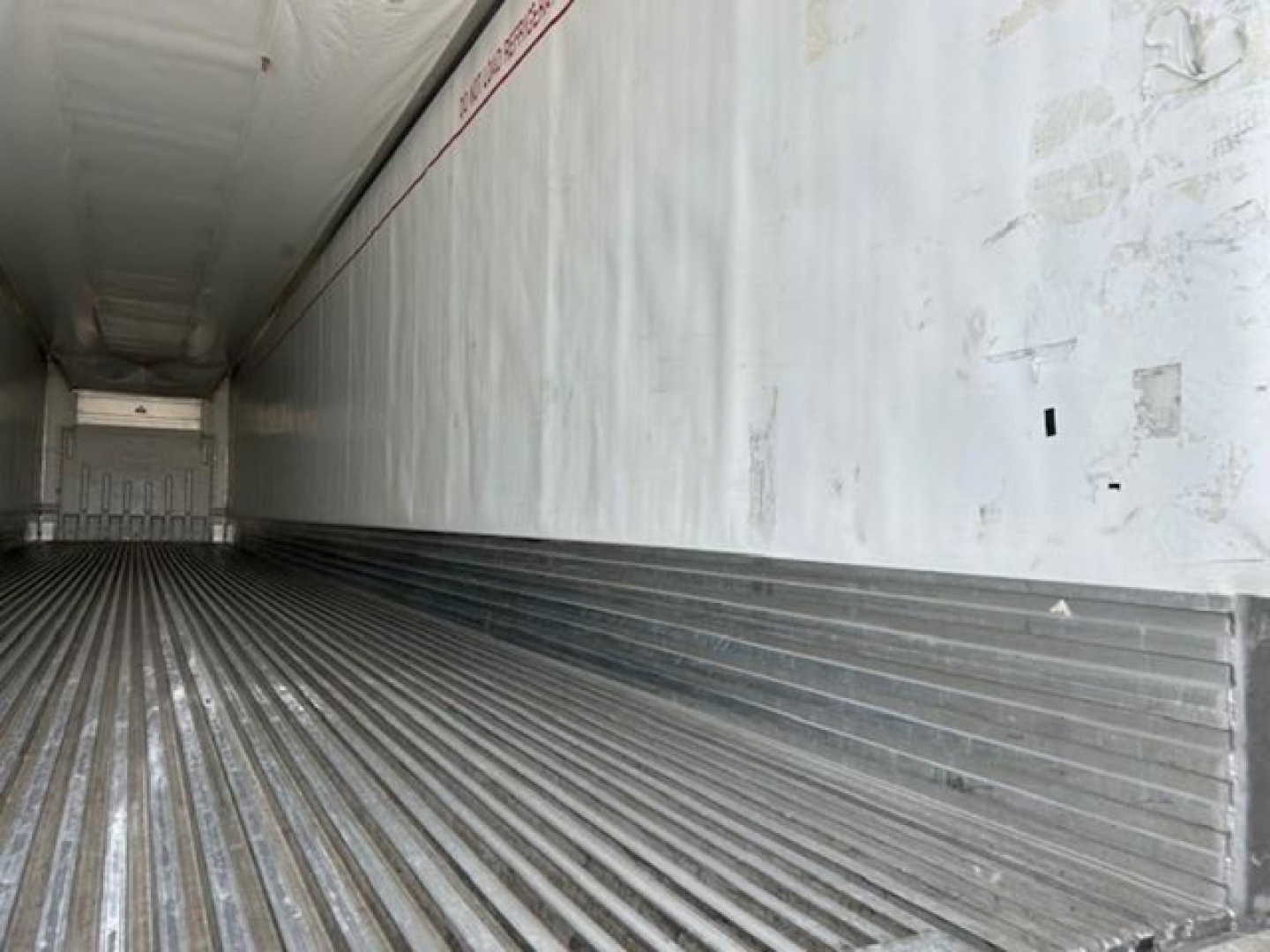 Refrigerated trailer interior with ribbed metal floor and white walls viewed from rear.