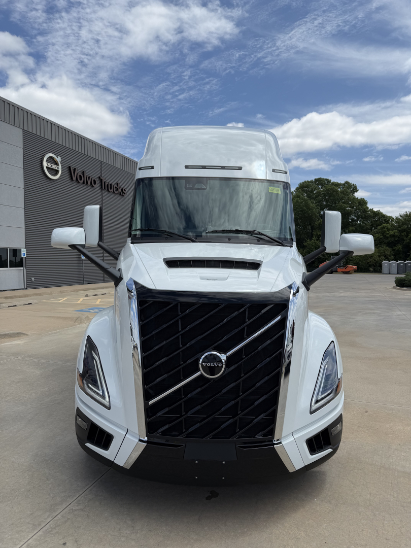 Front view of a white Volvo VNL64T860 truck in a dealership lot showing the large black grille with Volvo emblem, daytime sky.