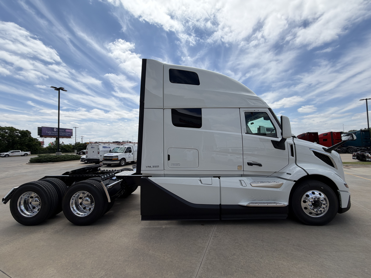 Truck cab side view showing Volvo VNL64T860, large sleeper cab with curved window, tandem rear axles, white exterior, chrome wheels.