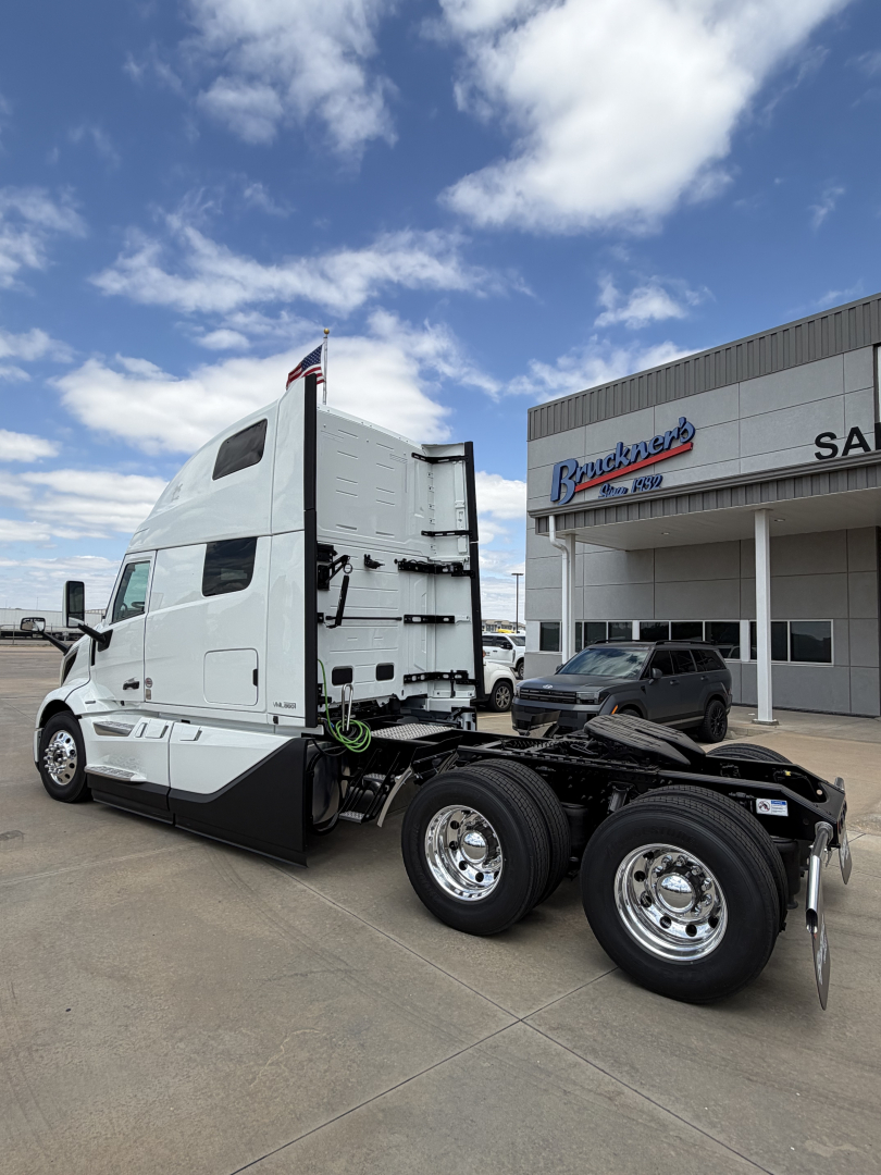 Volvo VNL64T860 heavy-duty truck tractor side view showing cab rear with fifth wheel and dual rear axles, white with chrome fuel tanks and a dealership building in background.