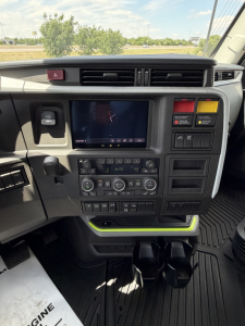 Dashboard of a Volvo VNL truck cab showing center console with touchscreen display and climate controls, hazard button, two vertical storage bays, cup holders, and yellow-green accents.