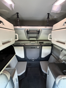 Volvo VNL64T860 sleeper cab interior showing overhead storage, ladder rack, and seating area in neutral tones.