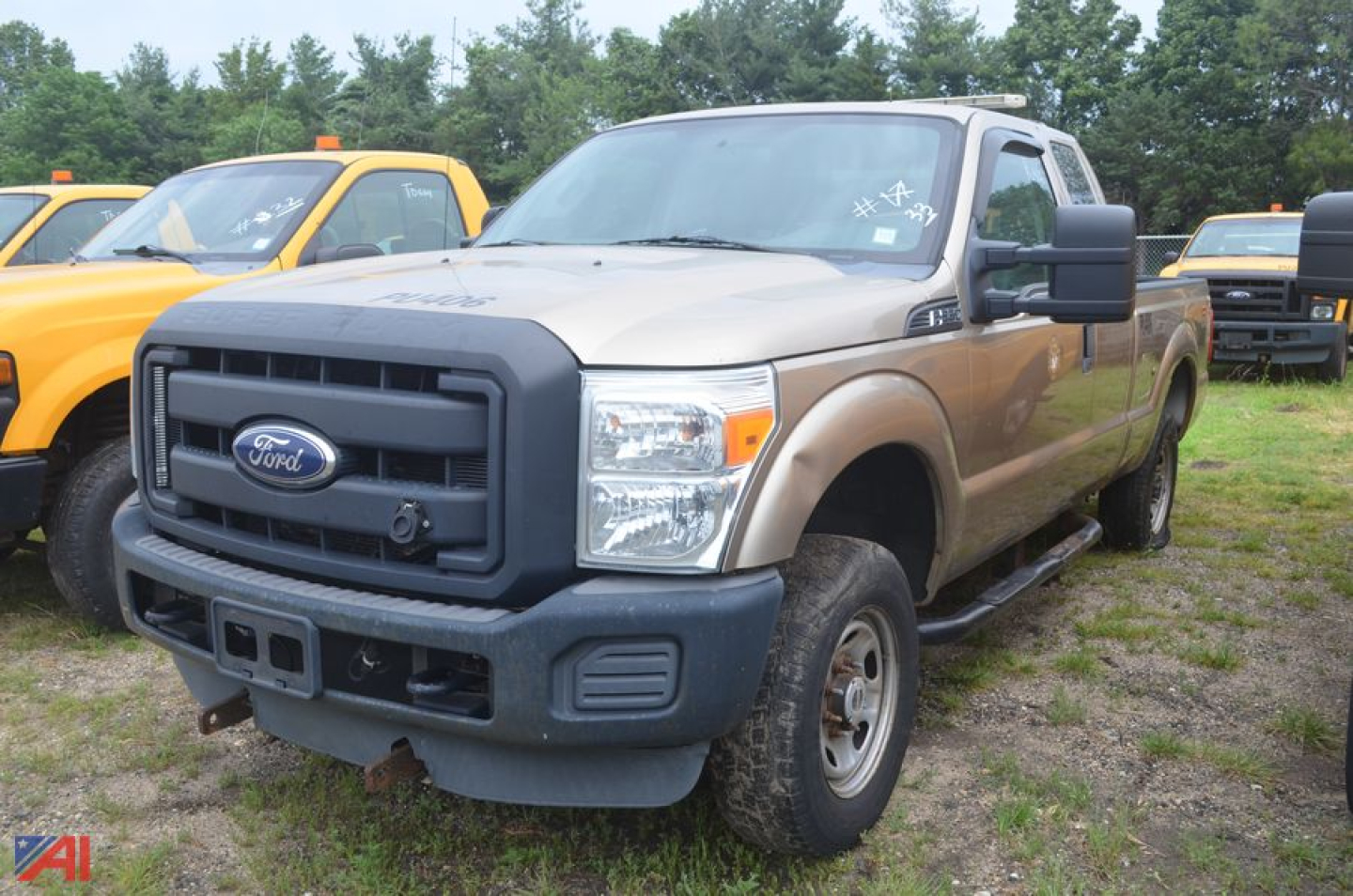 Ford F-250 Super Duty pickup truck extended cab in beige with black front bumper and grille, parked on grassy lot among other trucks.