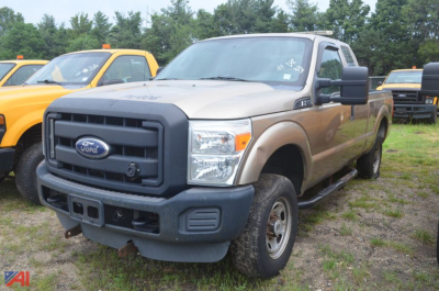 Ford F-250 Super Duty pickup truck extended cab in beige with black front bumper and grille, parked on grassy lot among other trucks.