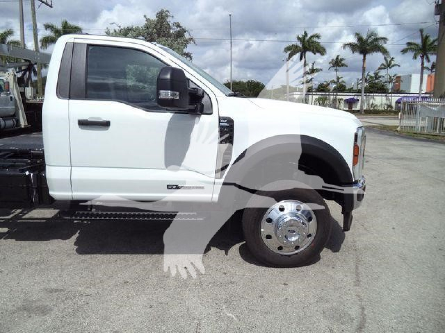 Ford F-550 single cab pickup truck side view showing white exterior, dual rear wheels, large chrome front wheel, and chassis cab with flatbed/rollback equipment in a dealership lot.