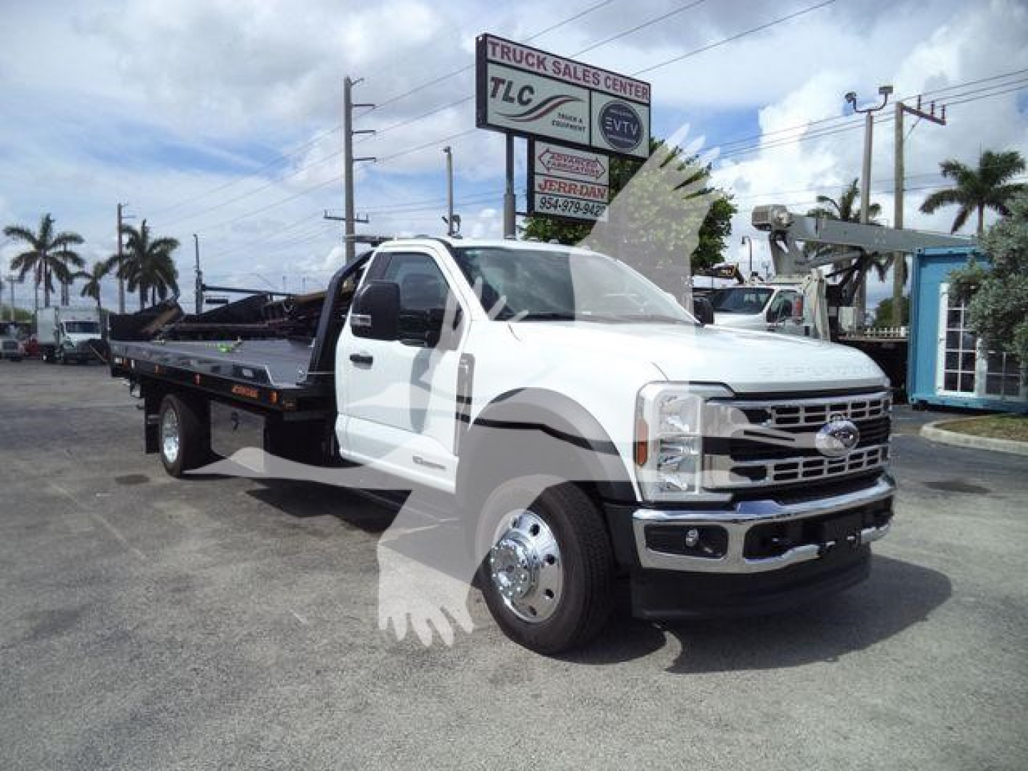 Ford F-550 rollback truck with white cab and flatbed, visible signage in background, roadside dealership lot.