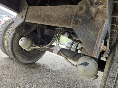 Underneath view of a 2016 utility combo flatbed trailer showing suspension, leaf springs,-dirt and two circular air tanks, rust on frame.