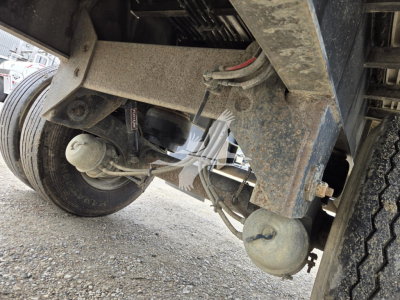 Trailer undercarriage showing suspension and wheel assembly with air lines and hoses; dirt and grime on metal frame; round trailer support component visible.