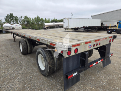 Flatbed trailer showing dual rear axles with wooden deck and rear mud flaps; reflective tape and taillights along side; stock trailer accents visible.