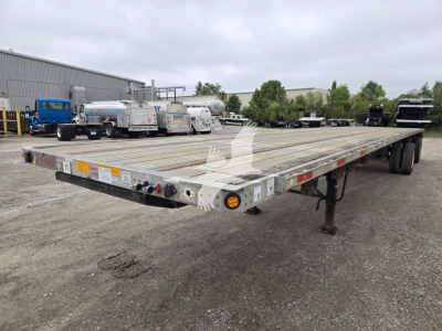 Flatbed trailer with long wooden deck showing rear lights and support legs; visible text includes stock decals and warning labels along the edge.
