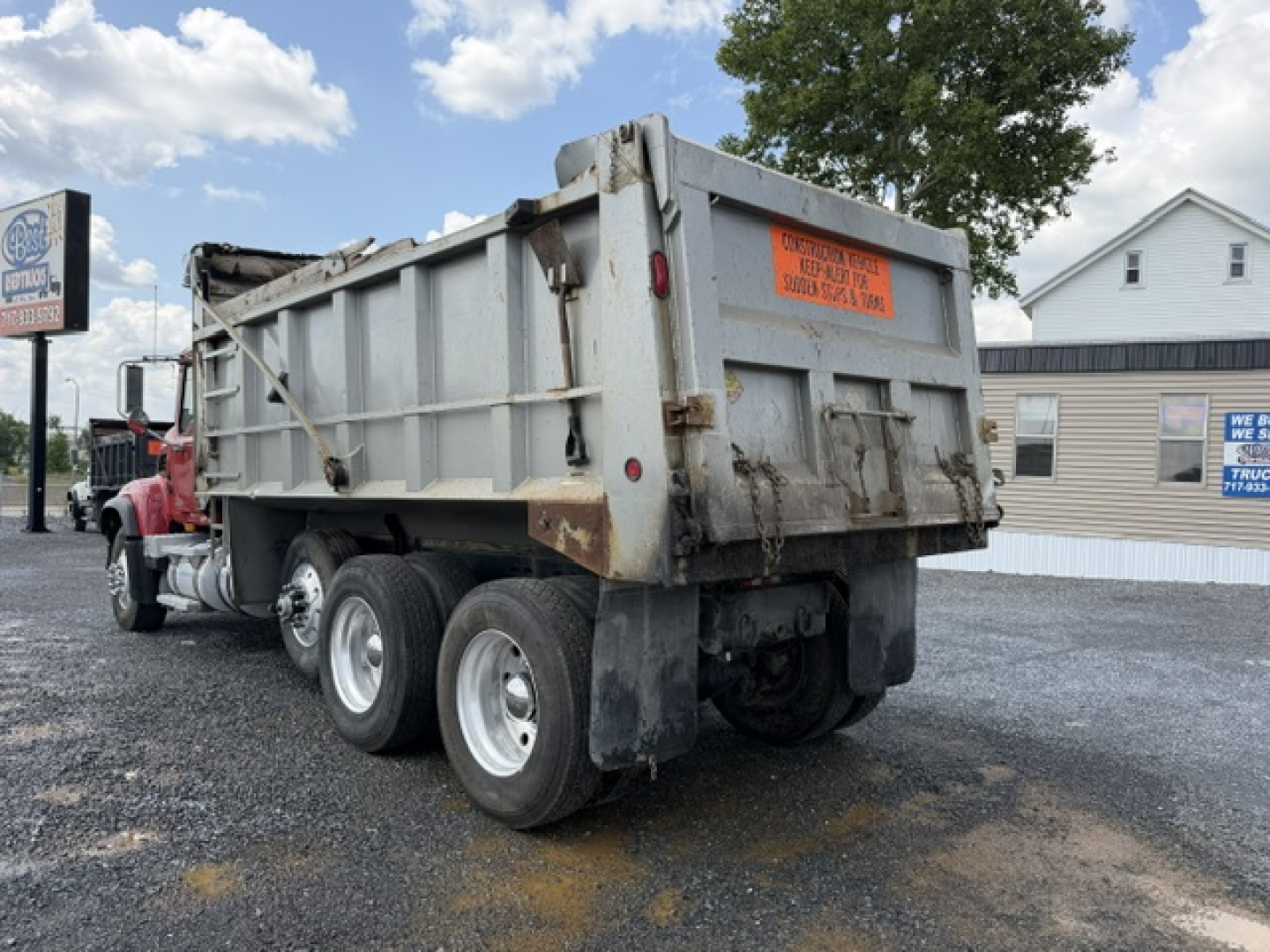 Dump truck bed showing rear and left side with orange caution label and dual rear axles on a Mack CV713.