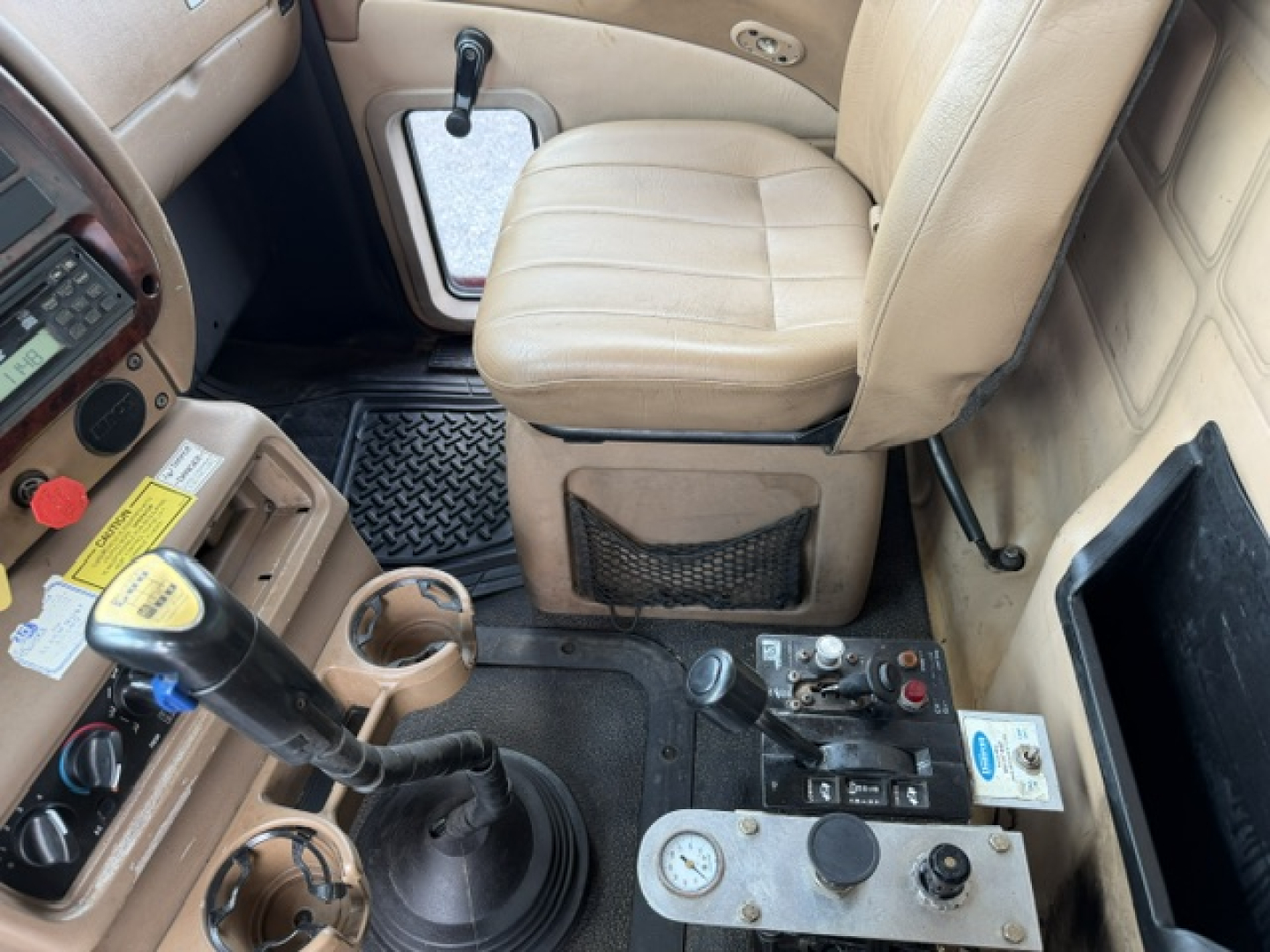 Cab interior of a 2004 Mack CV713 dump truck showing driver seat, gear shifter, steering wheel area, and center console with controls.