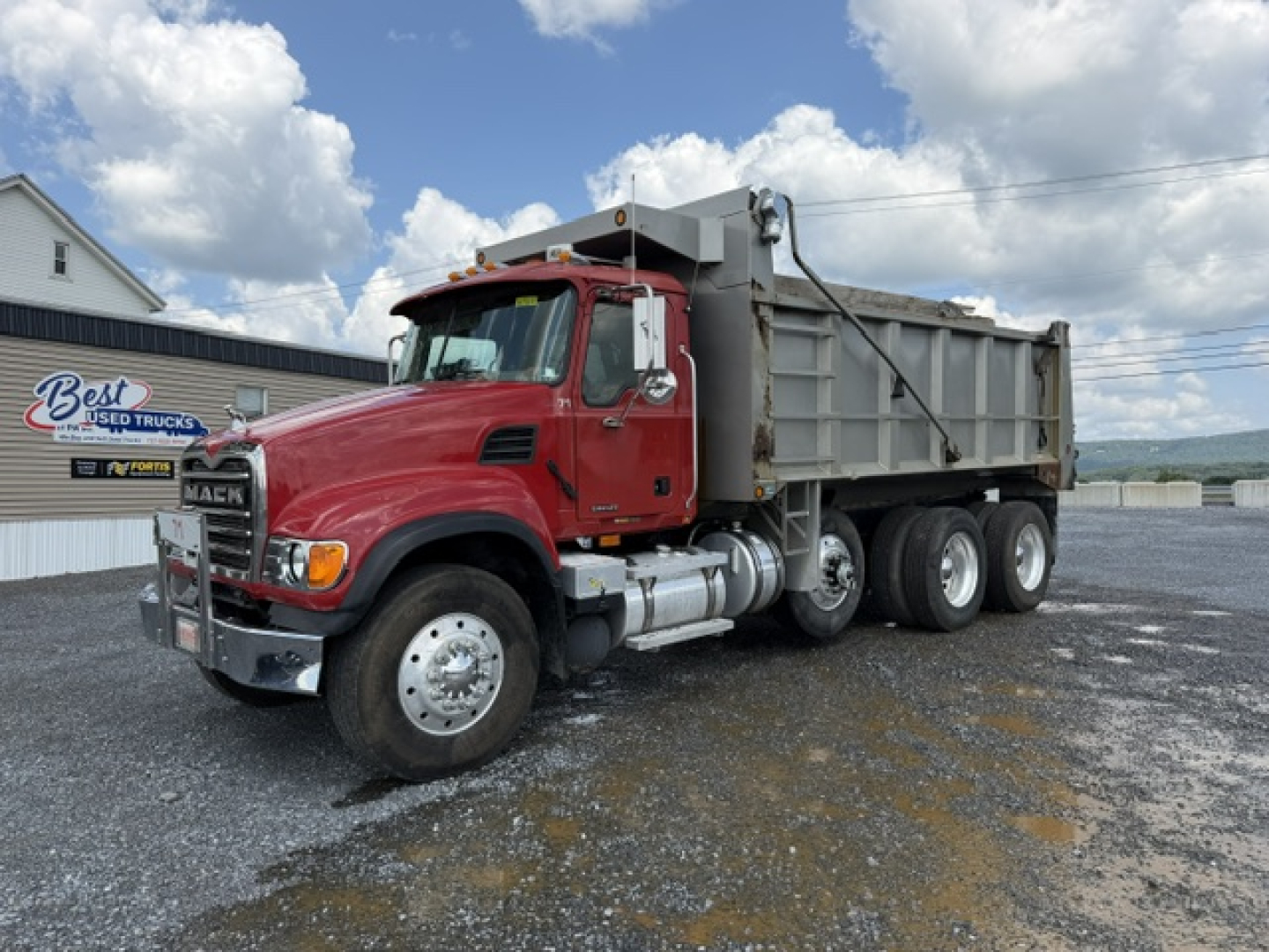Dump truck: red 2004 Mack CV713 with dump bed, side view showing front grille, dual exhaust, heavy-duty tires, and metal dump bed.