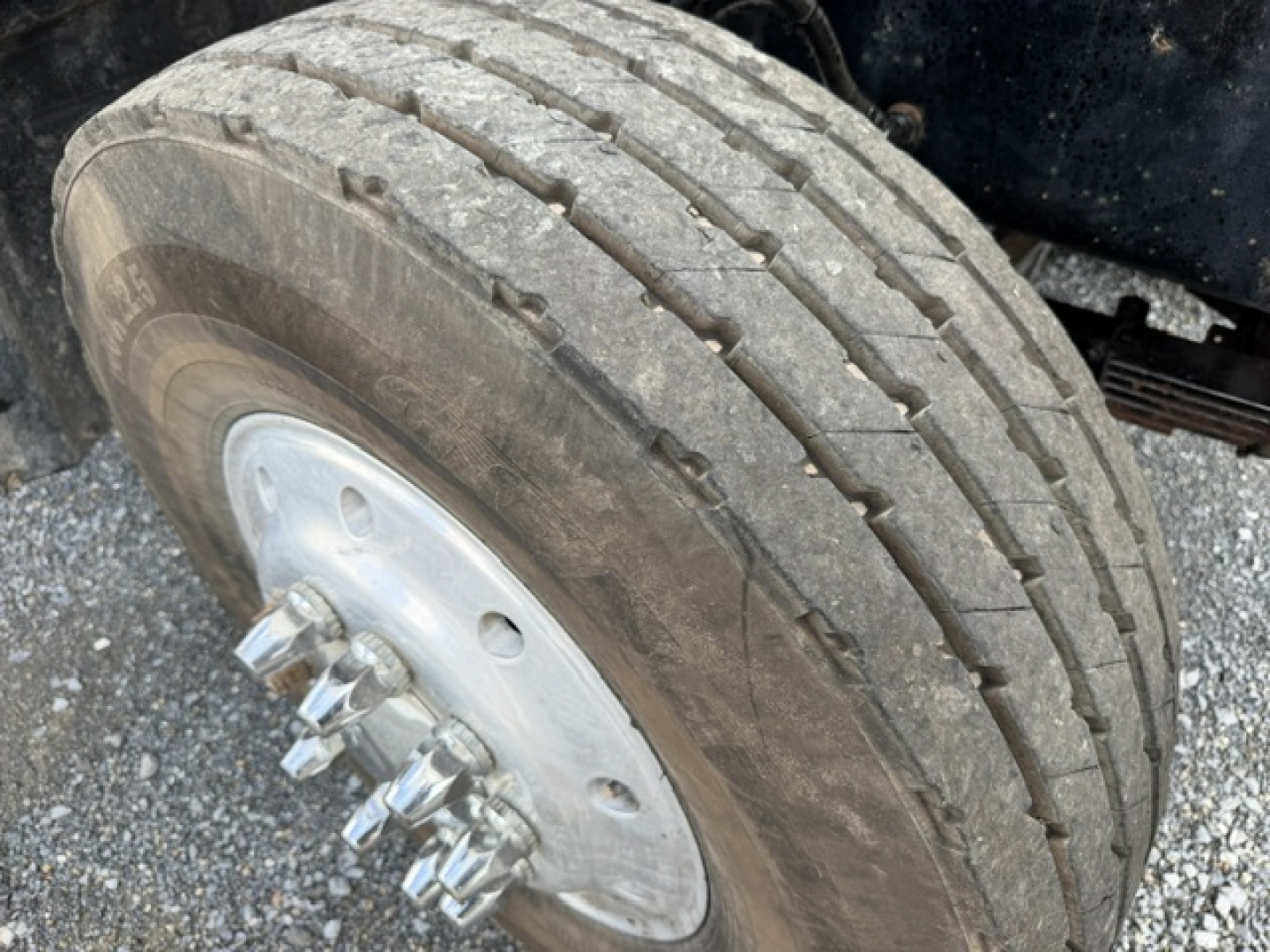 Dump truck wheel and tire close-up in-service showing dual rear axle with lug nuts, steel rim, and tread pattern.
