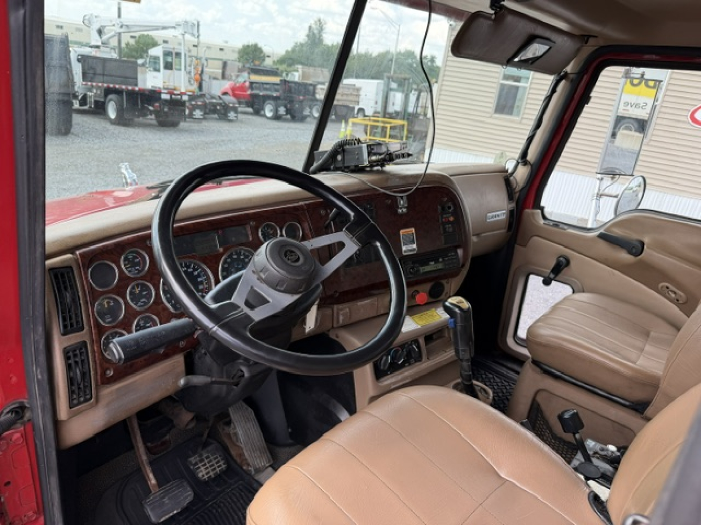 Cab interior of a 2004 Mack CV713 dump truck showing steering wheel, dashboard gauges, beige seats, and manual shifter.