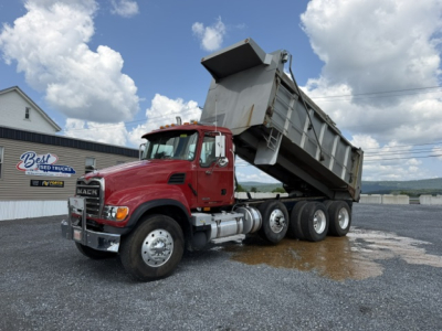Dump truck with raised bed showing Mack CV713 in red cab and silver dump body.