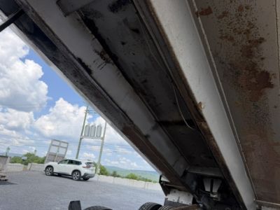 Rusted metallic underside of a Mack CV713 dump truck bed revealing structural beams and hydraulic components.