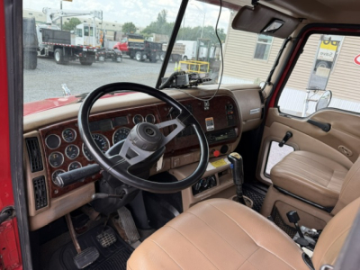 Cab interior of a 2004 Mack CV713 dump truck showing steering wheel, dashboard gauges, beige seats, and manual shifter.