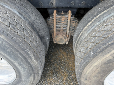 Dual rear tires with suspension and airbag/leaf spring assembly between them, showing rusty hardware and dirt in the center underside of a Mack CV713 truck.