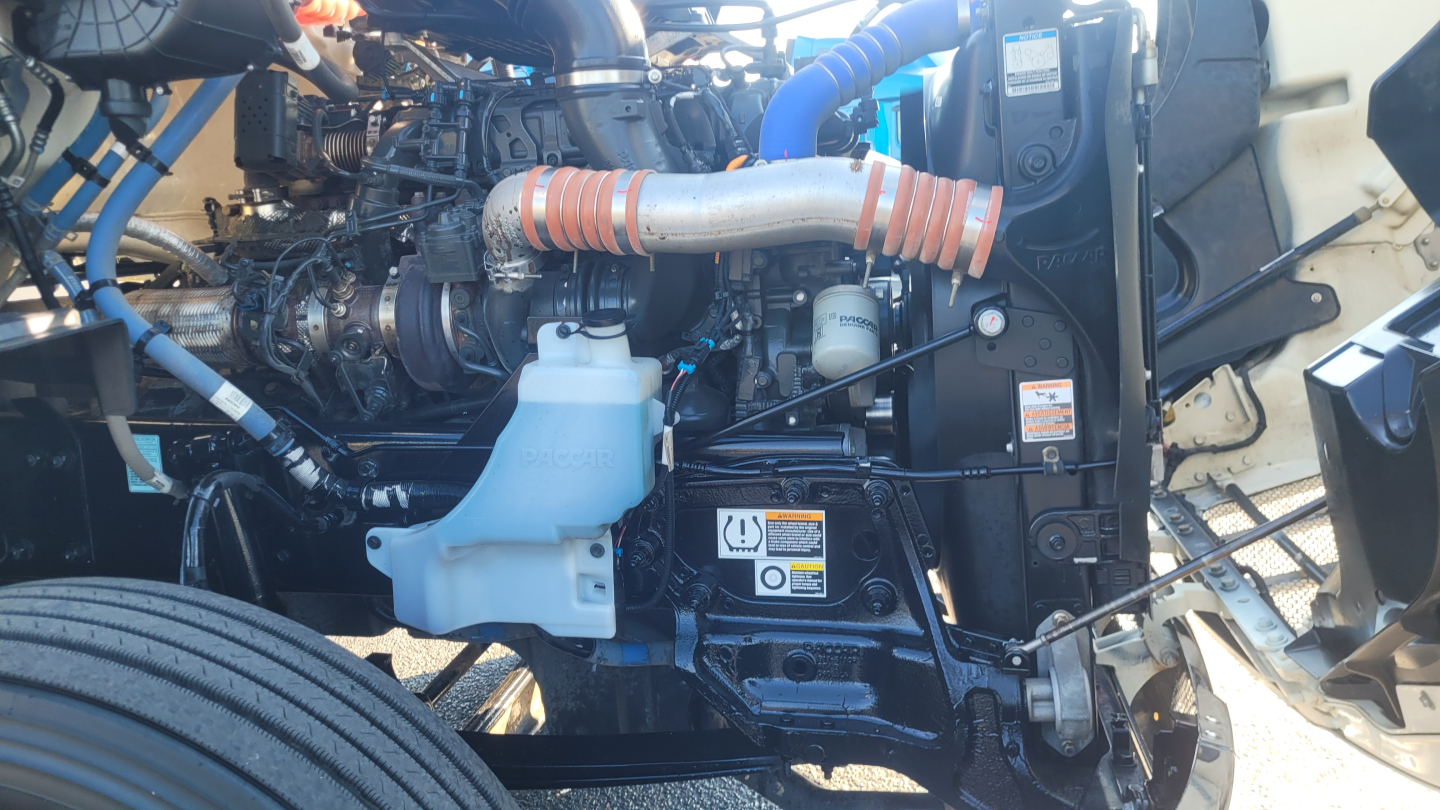 Peterbilt 579 engine bay showing coolant reservoir, turbo lines, hoses, and engine components.