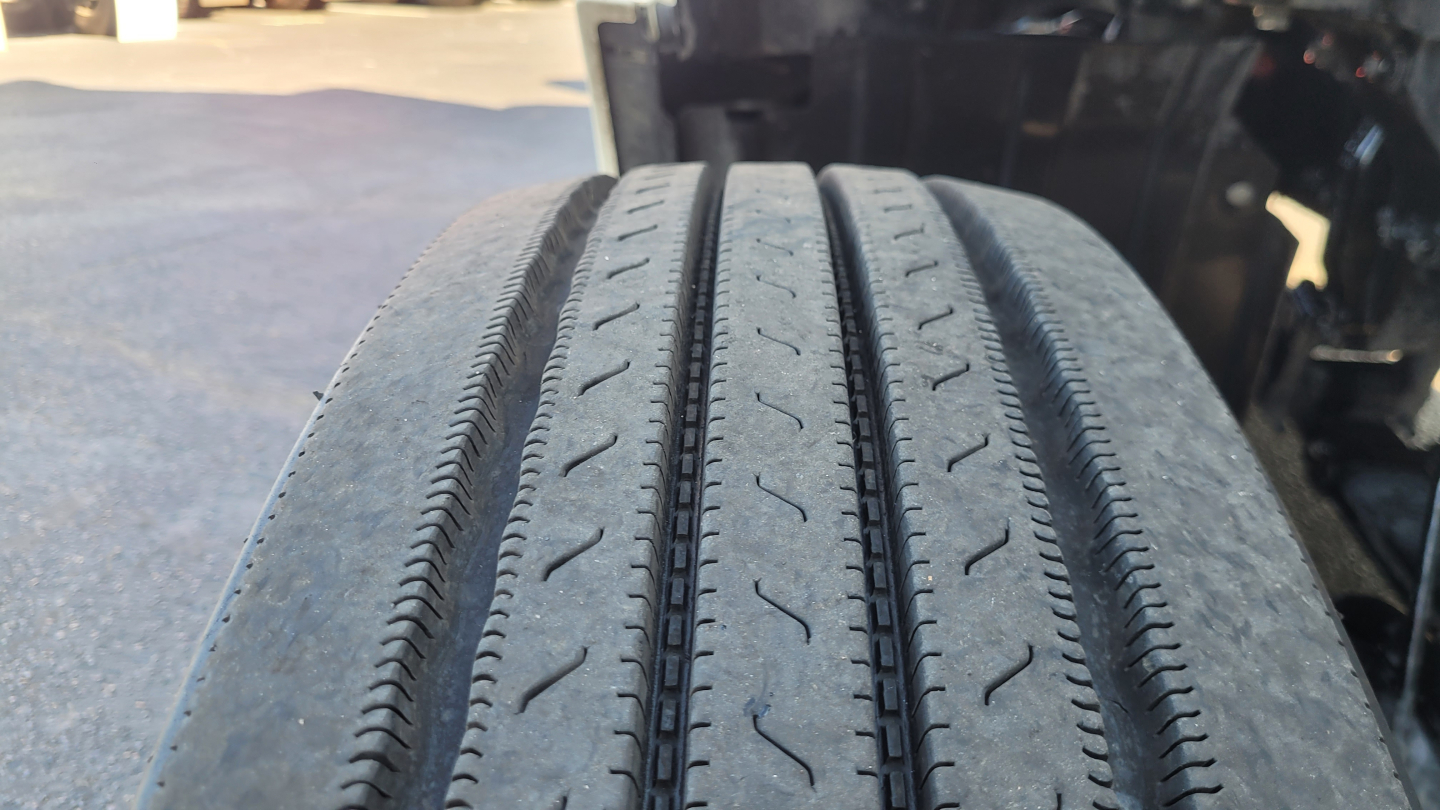 Truck wheel showing tread details on a Peterbilt 579’s front tire, close-up view with road grime and tire grooves visible.
