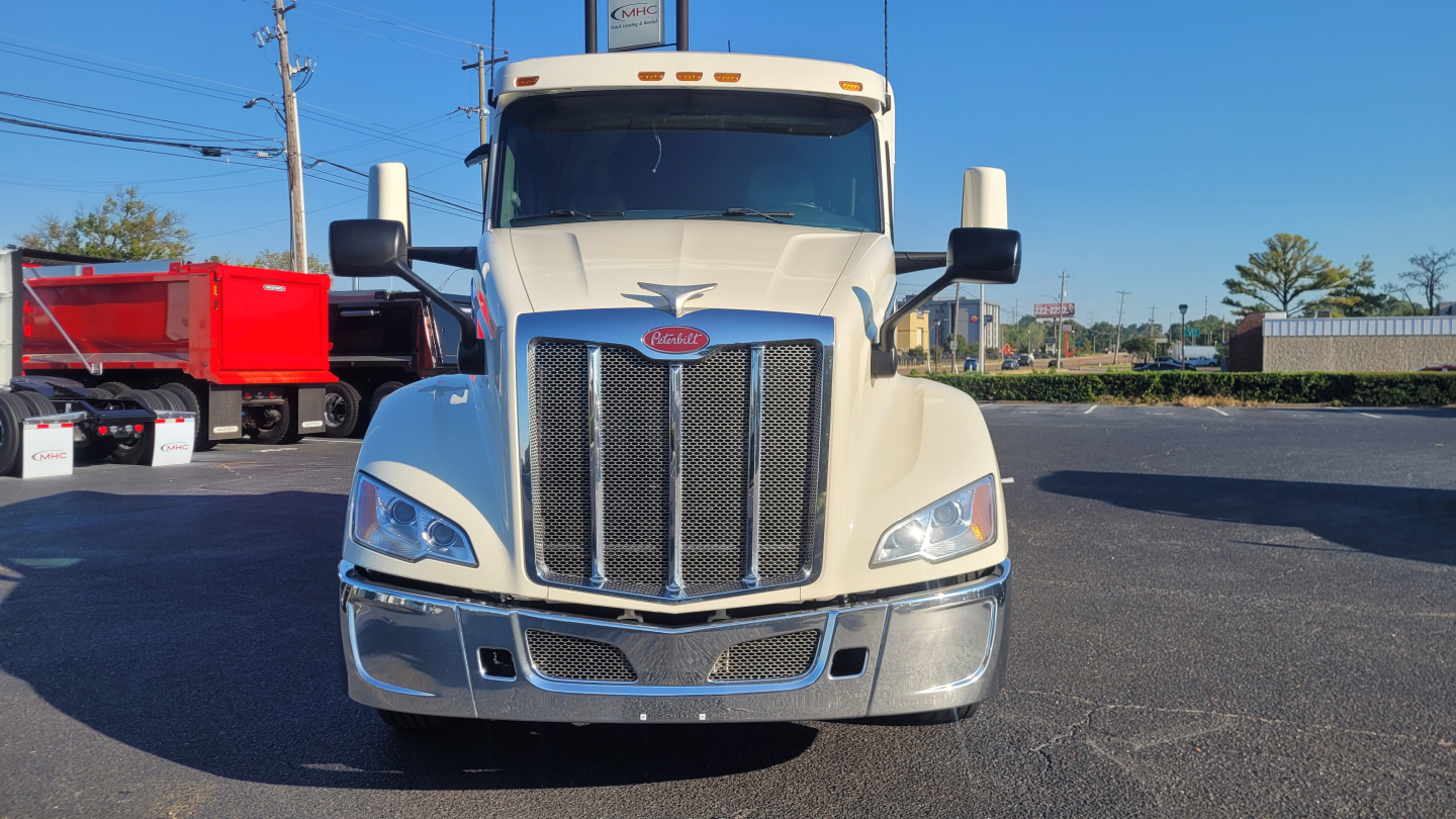Peterbilt 579 front view showing chrome grille, bumper, and Peterbilt emblem; headlamps and large side mirrors visible; truck is cream color with blue sky.
