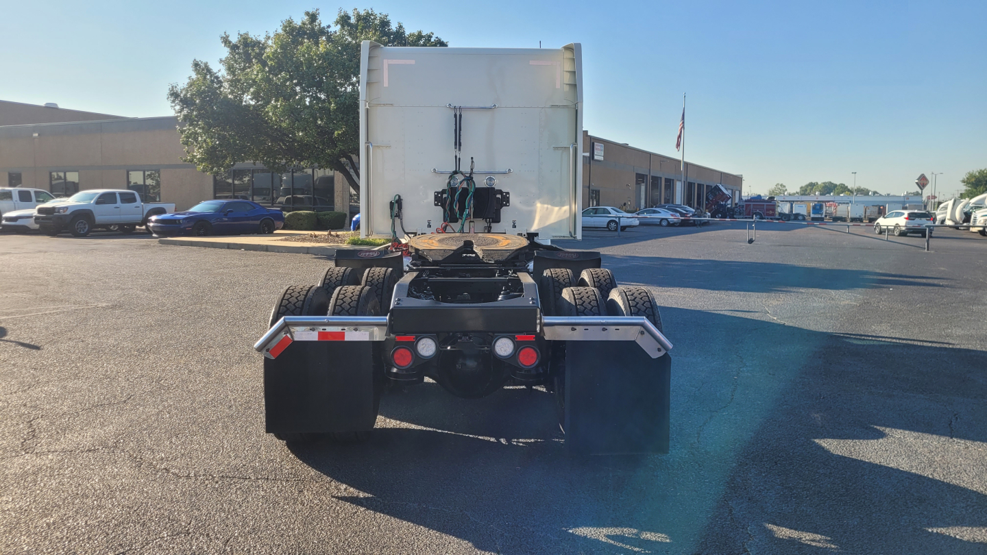 Peterbilt 579 rear view showing fifth wheel, rear tires, and chassis with trailer hookup; no cab in view; parking lot with other vehicles in background.