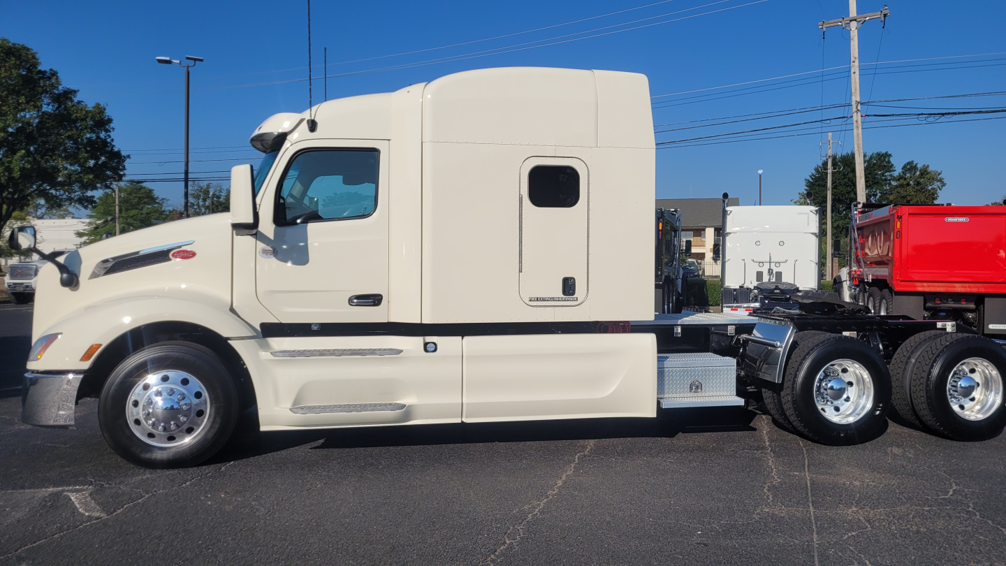 Peterbilt 579 sleeper cab tractor side view showing white exterior, chrome wheels, fuel tanks, and rear axle with dual wheels.