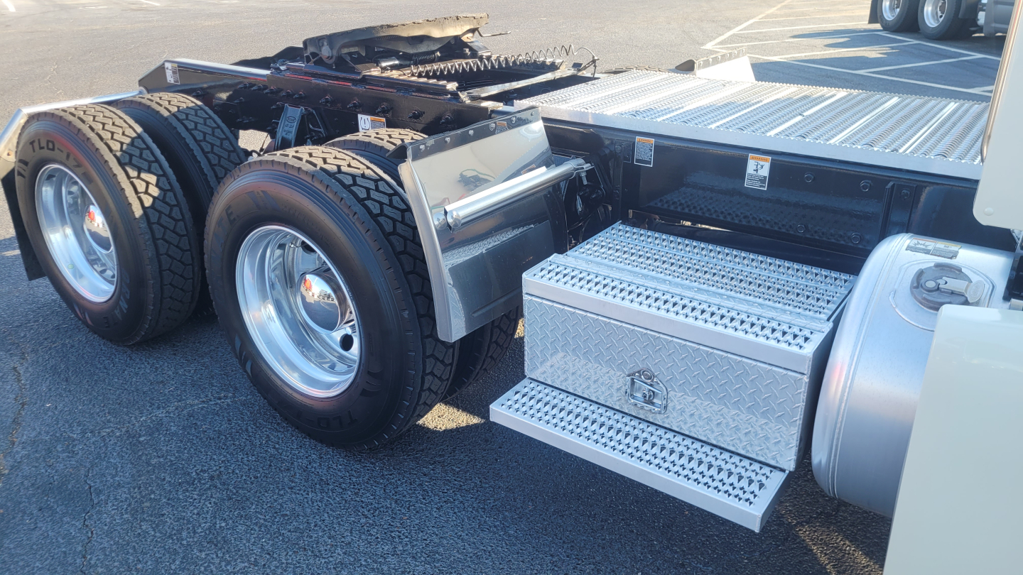 Peterbilt 579 tractor chassis with dual rear axles and aluminum diamond-plate step, showing side view of fuel and tool compartments.