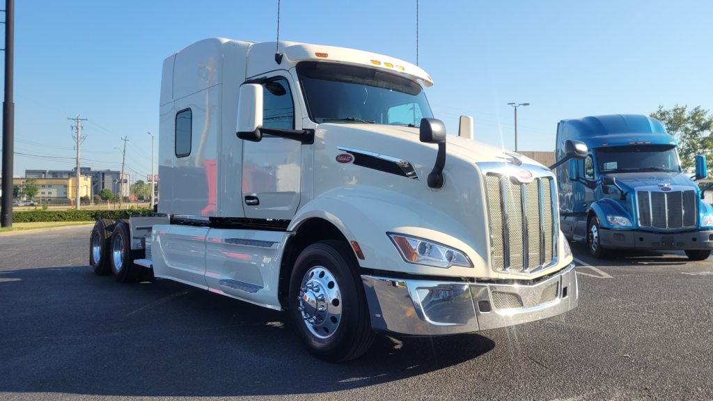 Peterbilt 579 conventional sleeper truck in silver/white parked in lot, front-left angle view with chrome grille and large mirrors