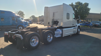Peterbilt 579 tractor in a lot, rear view showing tandem axles and fuel channels with chrome wheels.