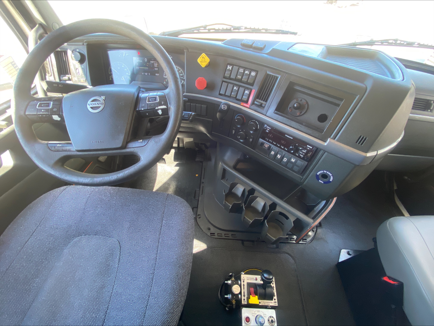Interior of a Volvo VNL300 cab showing the steering wheel, dashboard with control buttons, climate controls, and center console.