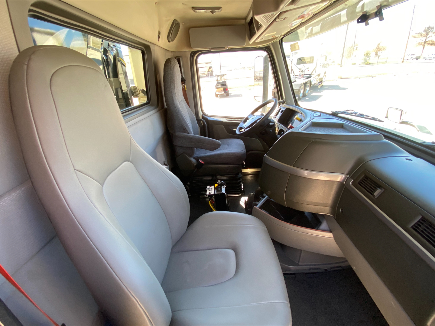 Cab interior of a 2021 Volvo VNL300 dump truck showing light gray front seats, dashboard, steering wheel, and center console.