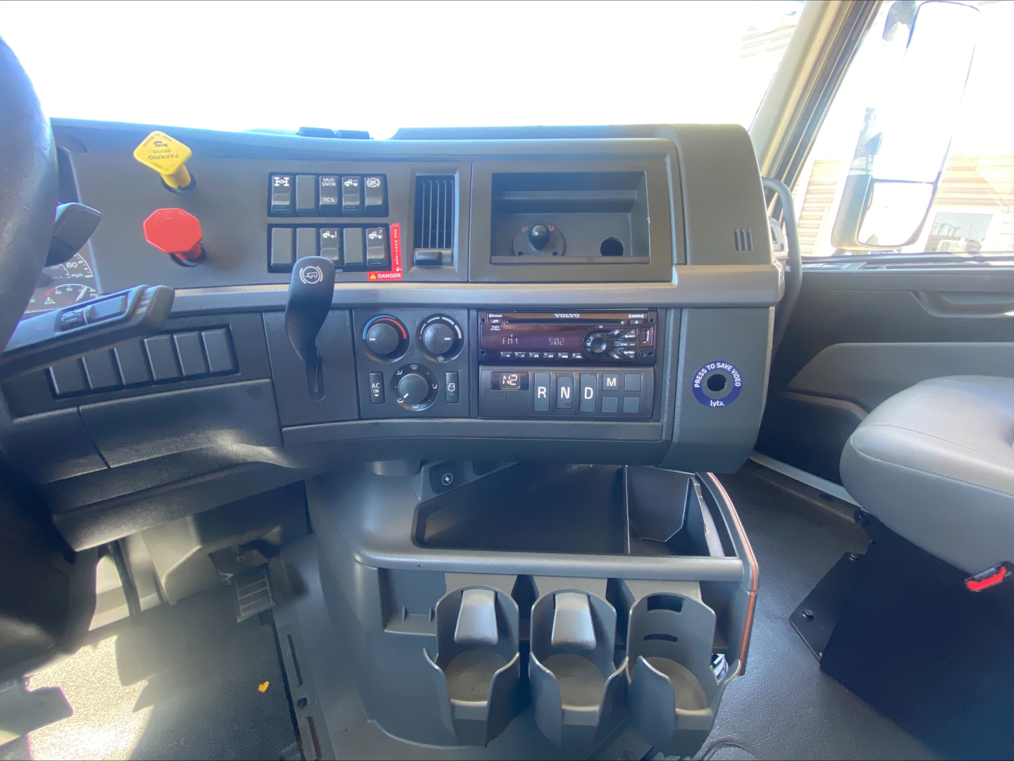 Dash area of a Volvo VNL300 interior showing switches, gear selector, climate controls, cup holders, and storage compartments