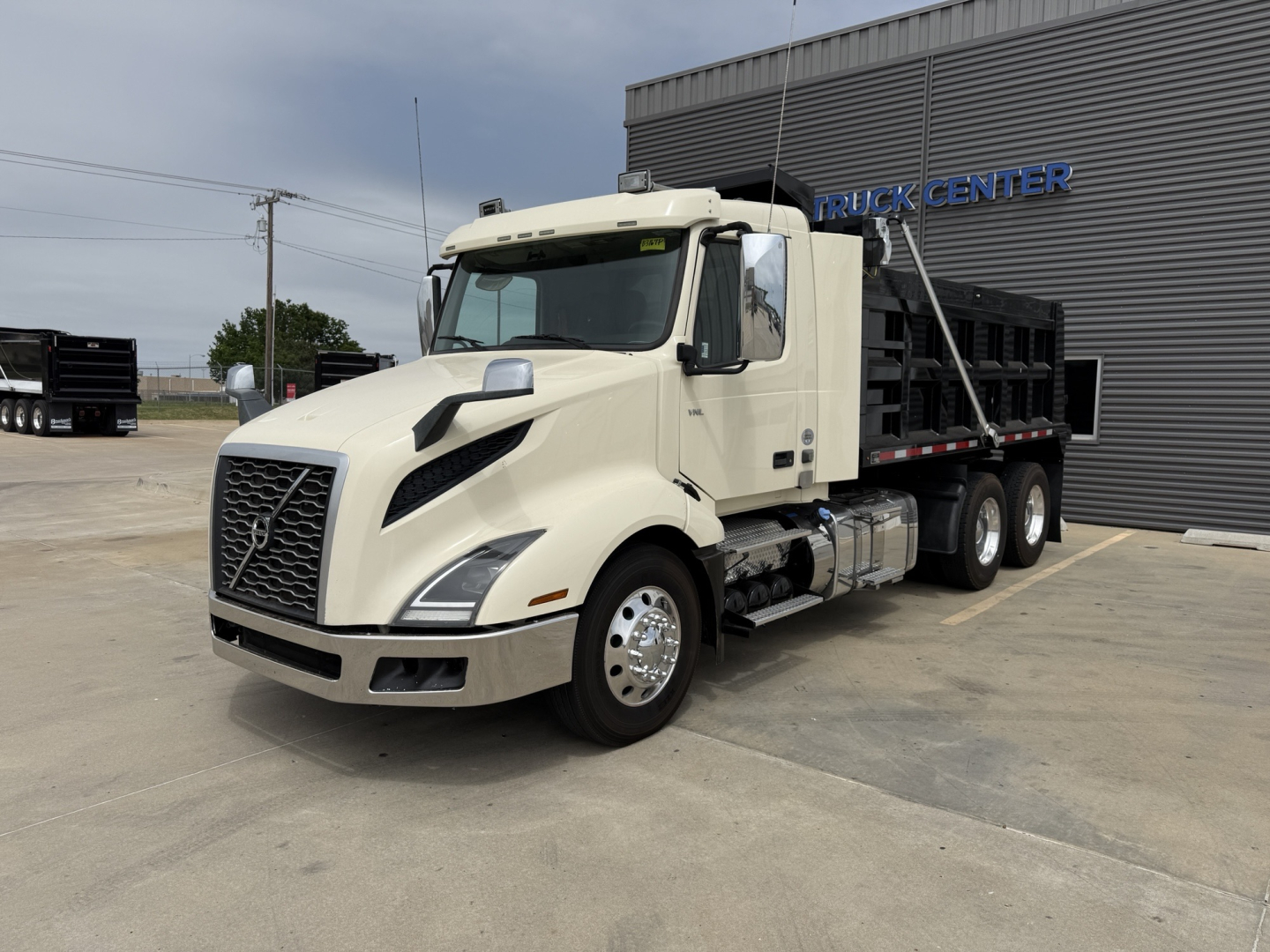 Volvo VNL300 dump truck in light tan color, front-left view, with Volvo emblem grille and dump bed visible.
