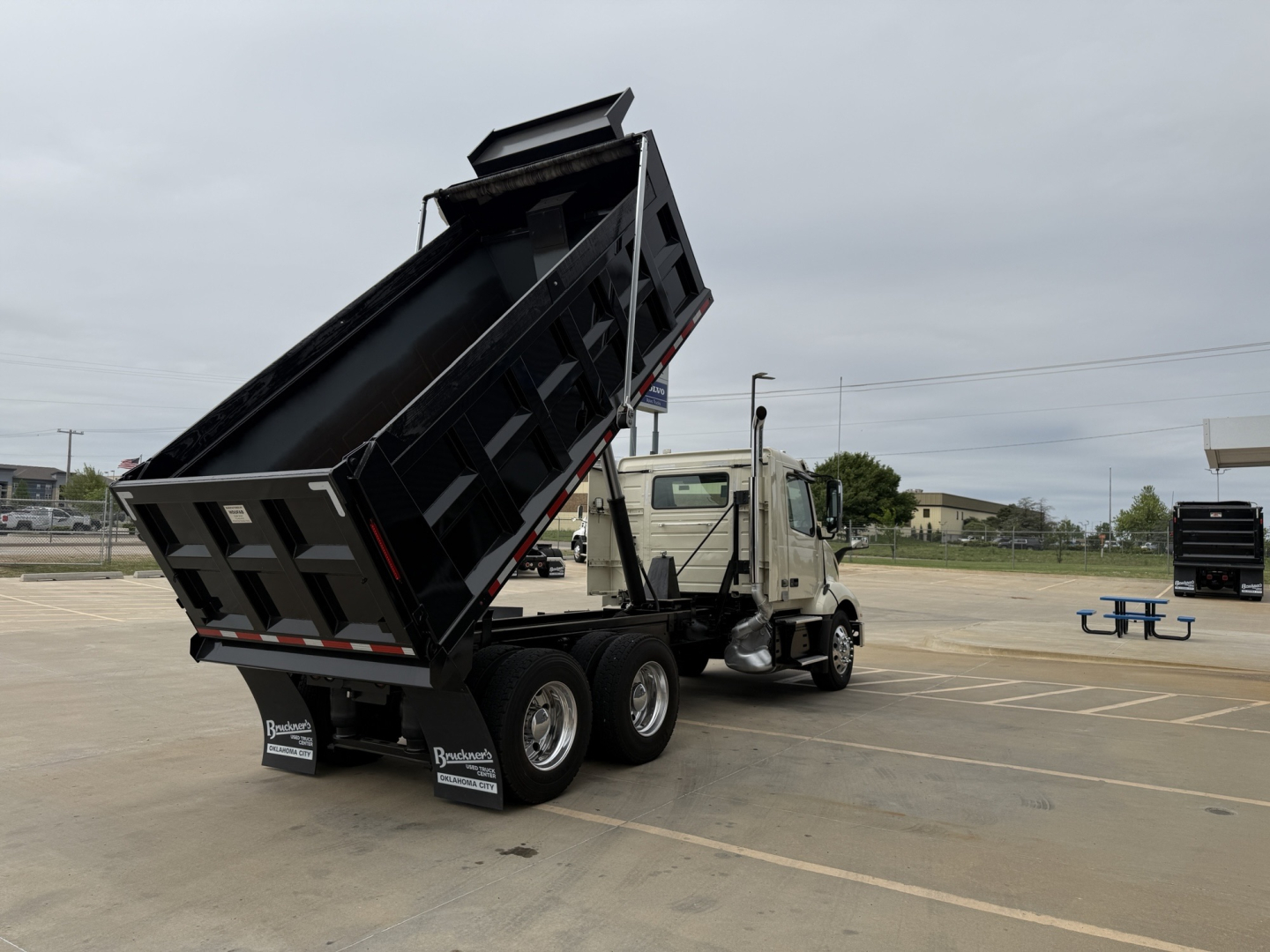 Volvo VNL300 dump truck in a parking lot with its bed raised for dumping.
