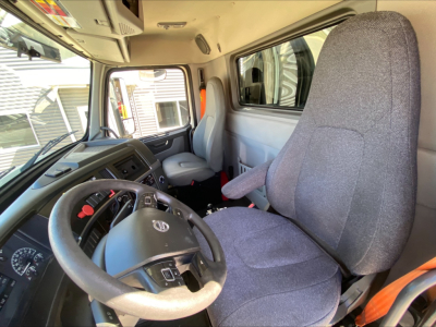 Truck cab interior showing steering wheel, driver seat, and dashboard of a Volvo VNL300 with fabric seats and gray color scheme.