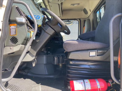 Volvo VNL300 cab interior showing steering wheel, driver seat, and dashboard with warning label; red fire extinguisher on floor; gray step under seat; light entering from open door.