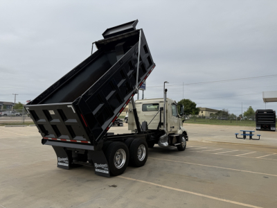 Volvo VNL300 dump truck in a parking lot with its bed raised for dumping.